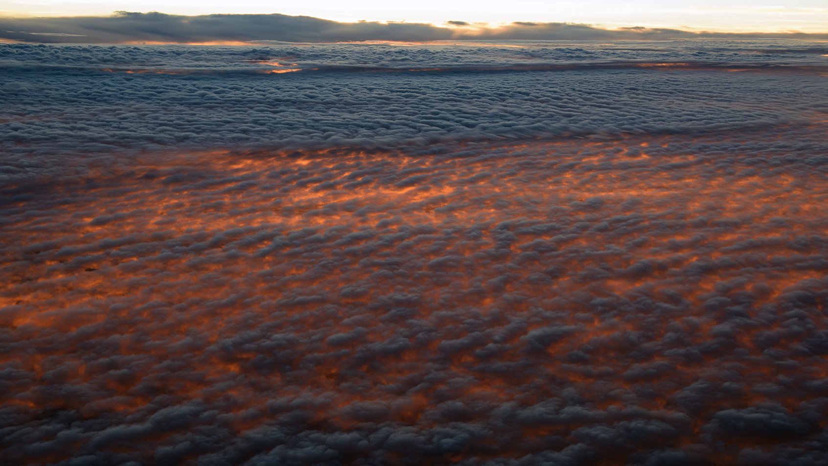 Sunrise between the Pacific marine layer cloud and upper level cloud. Taken from 38,000 feet,24 October 2015. 300 nm west of Los Angeles. (Photo: RDC)